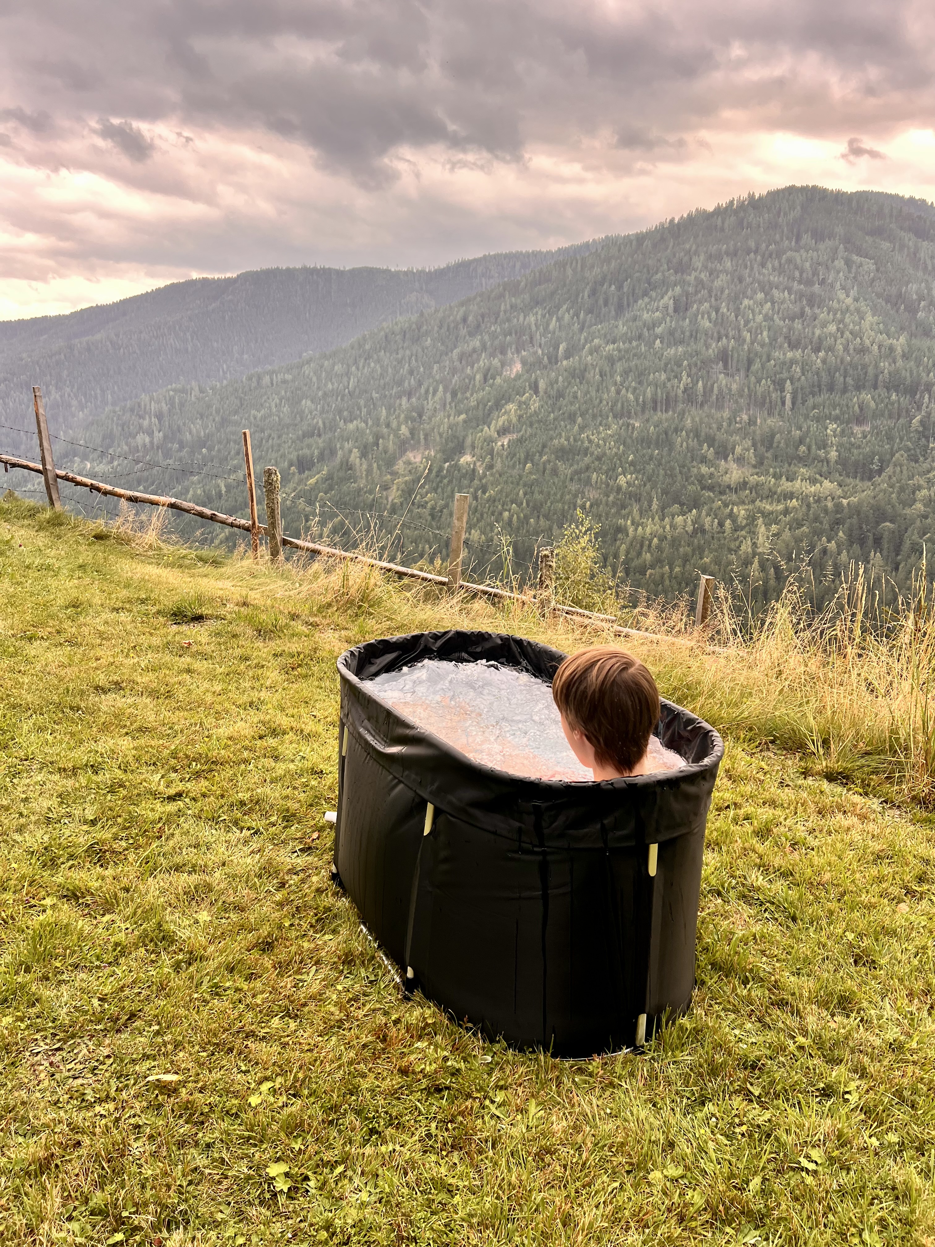 Faltbarer Eisbadezuber im Garten der alm44 mit Blick auf die bewölkten Berge